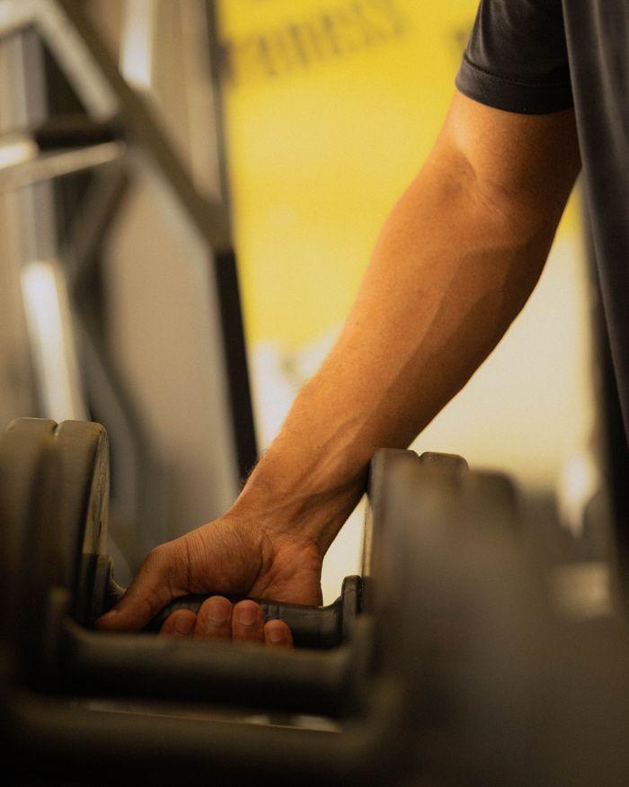 A muscular arm lifting a dumbbell in a gym setting, emphasizing strength and fitness.